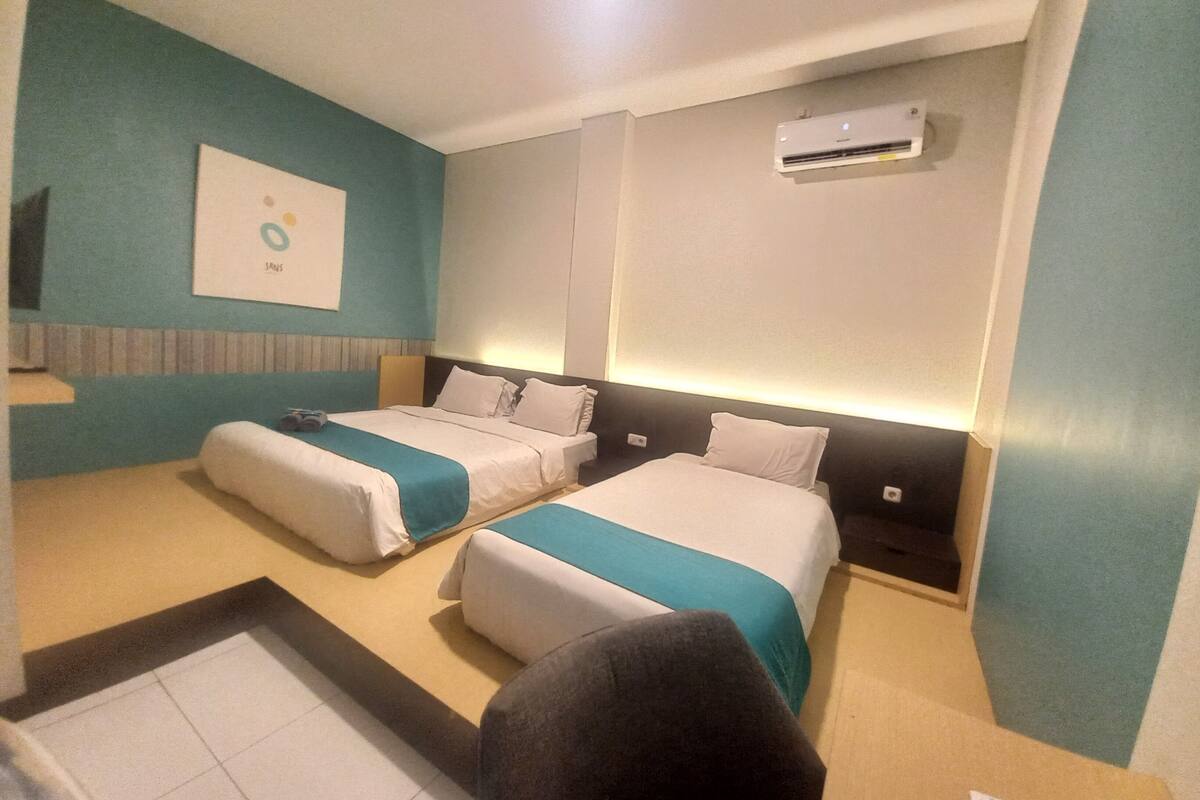 Hotellihuone, jossa on kaksi sänkyä, seinään asennettu ilmastointilaite ja seinällä oleva taulu.