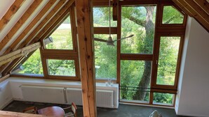Una habitació amb sostre inclinat, grans finestres, un radiador i una cadira.