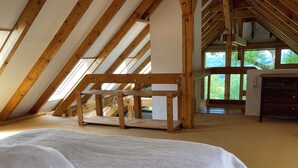 Habitació amb sostre inclinat, un llit amb coixí floral, una banca de fusta i un taulell.