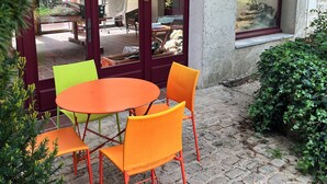 A patio with a round table and four chairs, a stone-paved ground, and a building with arched windows and a stone facade. - Maison de la Couturière (Collan)
