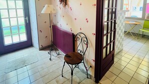 A room with a tiled floor, a radiator, a chair, a lamp, and a door leading to another room. - Maison de la Couturière (Collan)