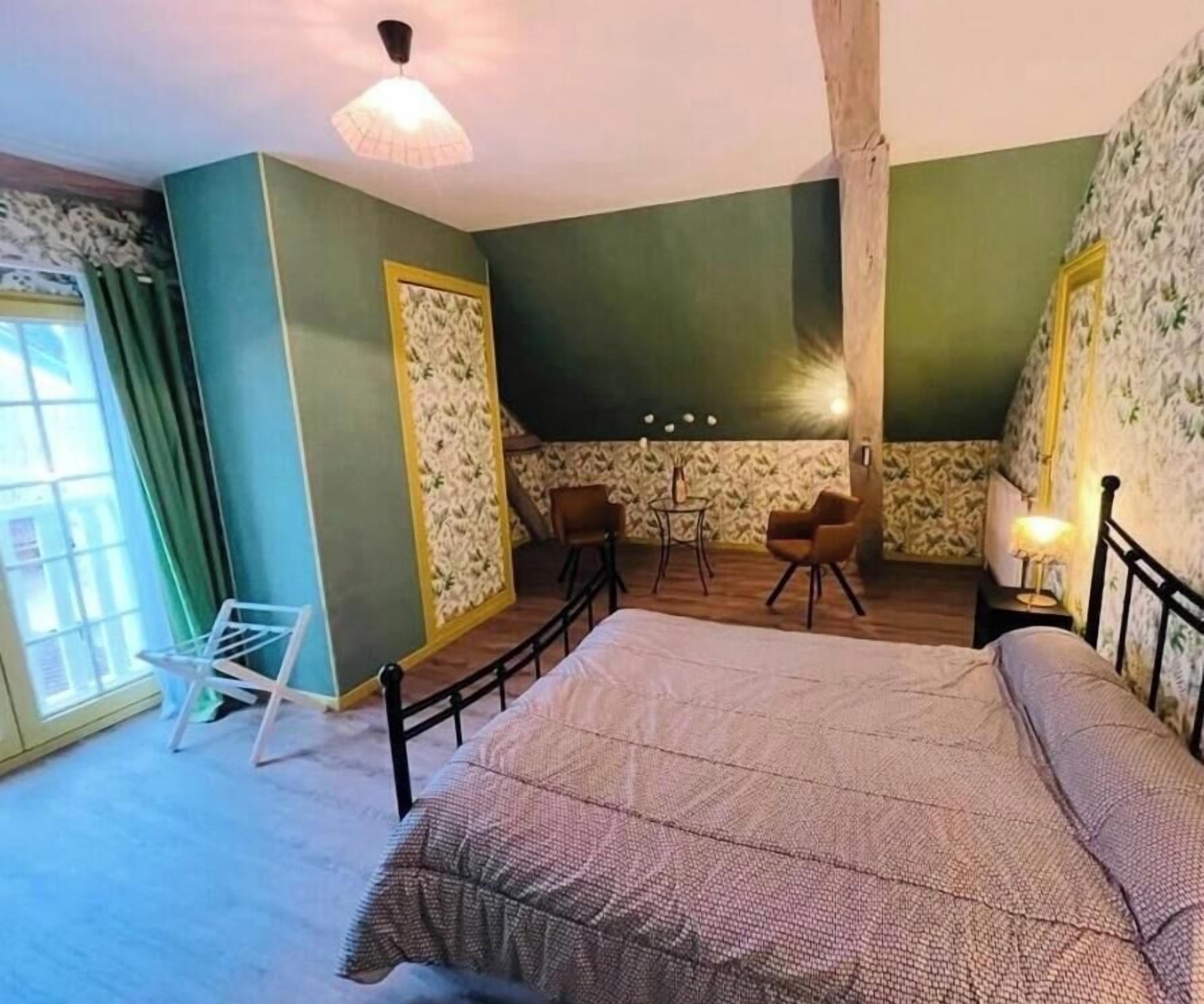 Een slaapkamer met een groot bed, twee stoelen, een tafeltje en een raam met gordijnen.
