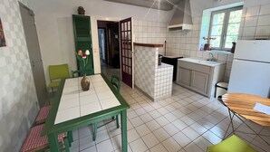 A kitchen with a dining area, including a table with chairs, a vase with flowers, and a refrigerator. - Maison de la Couturière (Collan)