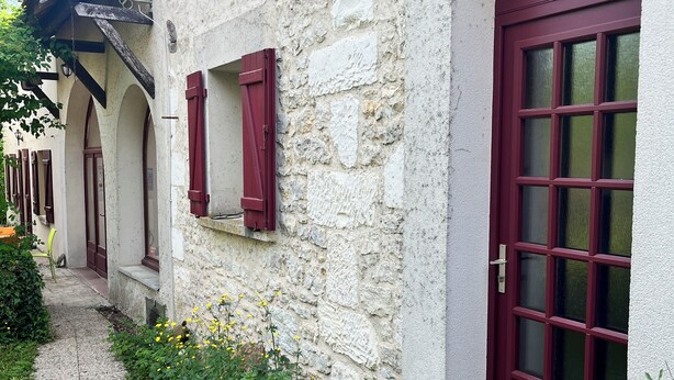 A stone building with a red door and windows, a gravel path, and a small garden area. - Maison de la Couturière (Collan)