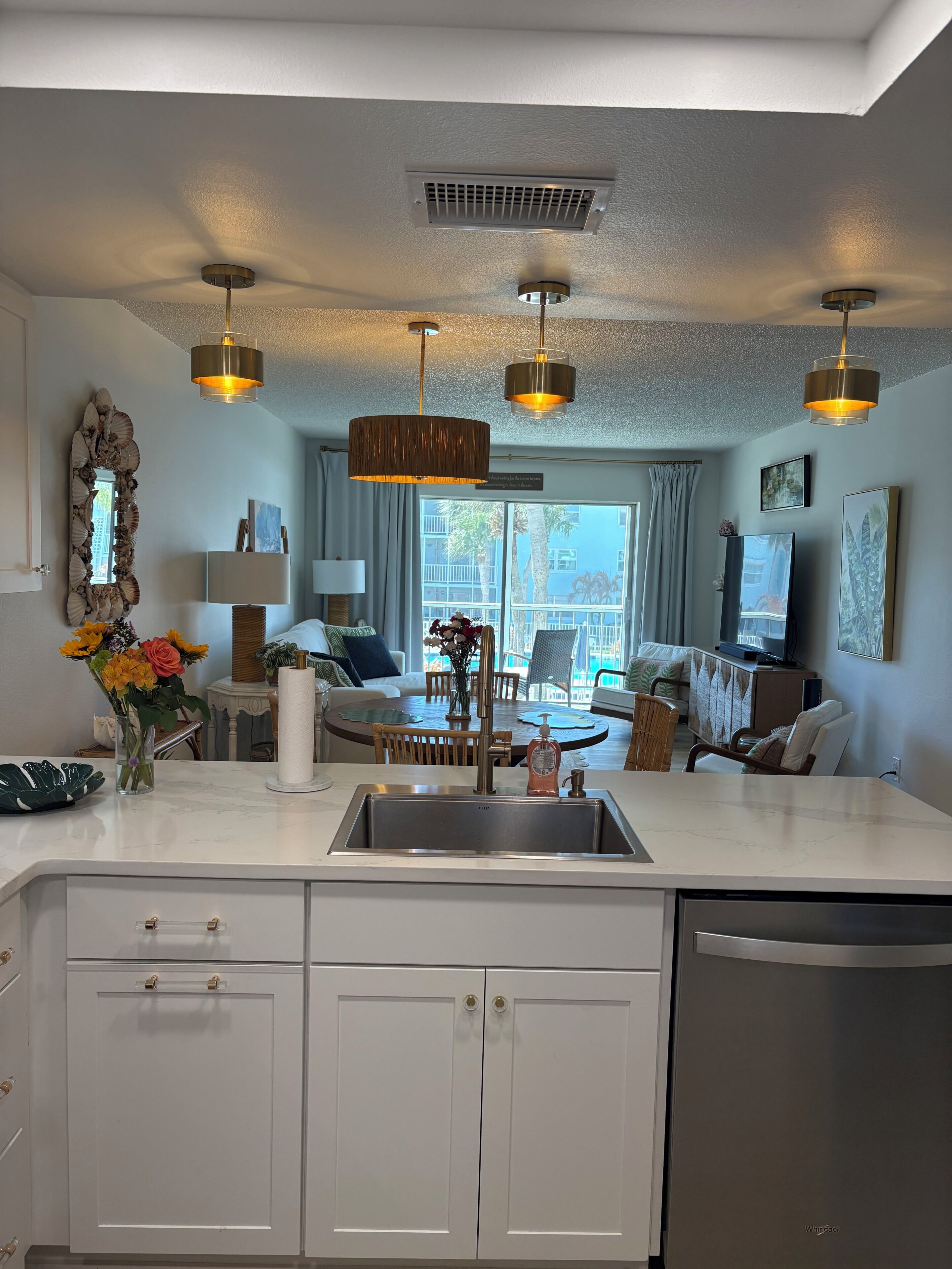 A modern kitchen with a central island, stainless steel appliances, pendant lighting, and a view of the living area.