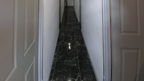 Um corredor com paredes brancas, piso de mármore preto e portas brancas.