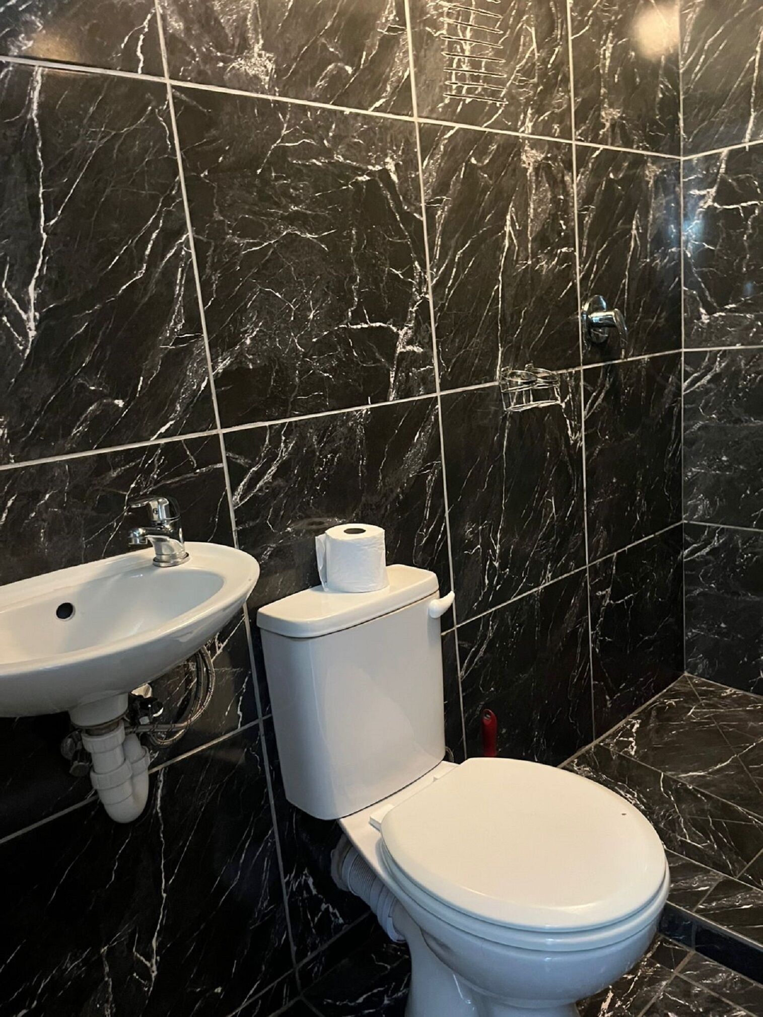 Une salle de bain avec un lavabo blanc, des toilettes et des carreaux de marbre.