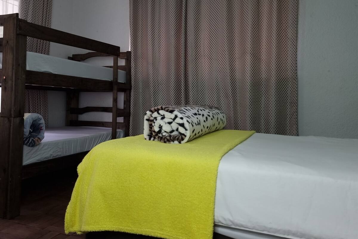 A room with bunk beds, a bed with a yellow blanket, and patterned curtains.