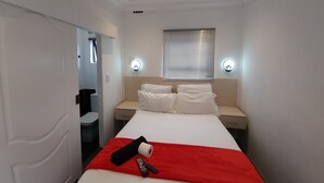 Quarto de hotel com uma cama, duas mesas de cabeceira, uma janela com persianas e duas luminárias fixadas na parede.
