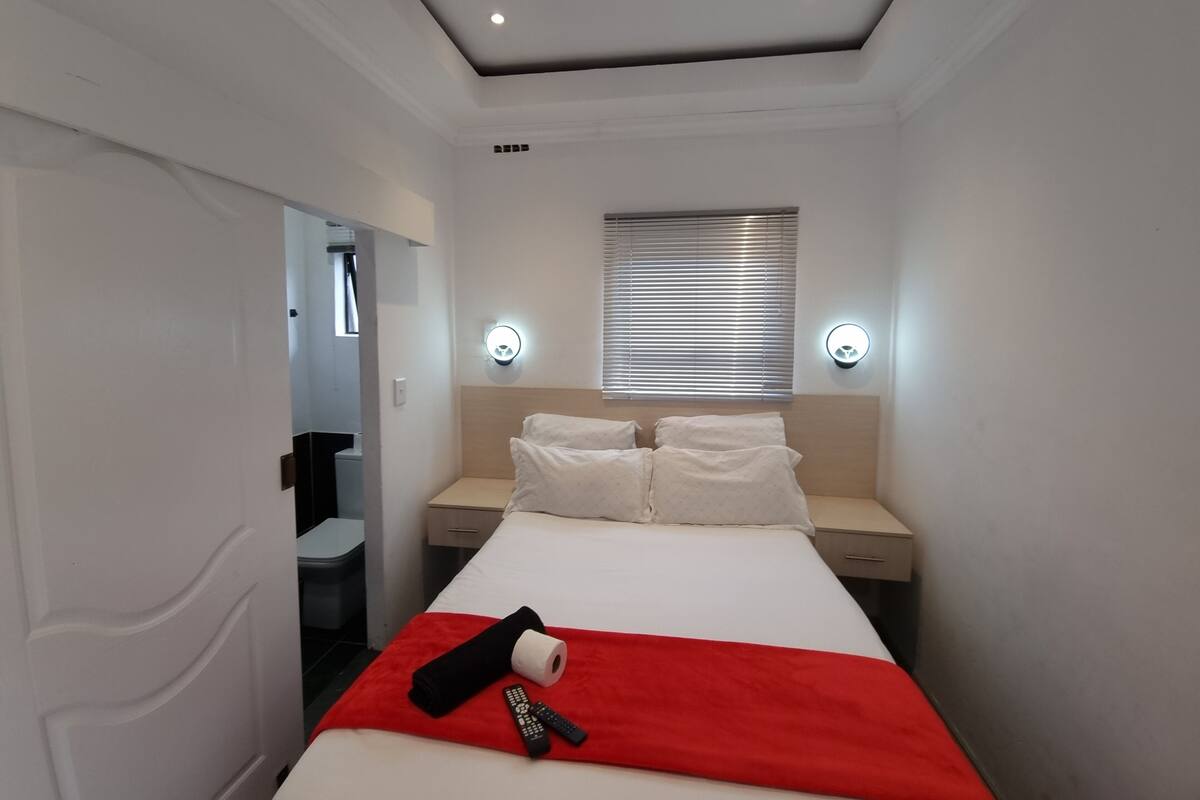 A hotel room with a bed, two bedside tables, a window with blinds, and two wall-mounted light fixtures.