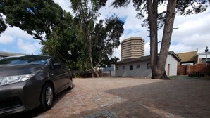 Um caminho de paralelepípedos com um carro estacionado, árvores e um edifício com telhado plano.