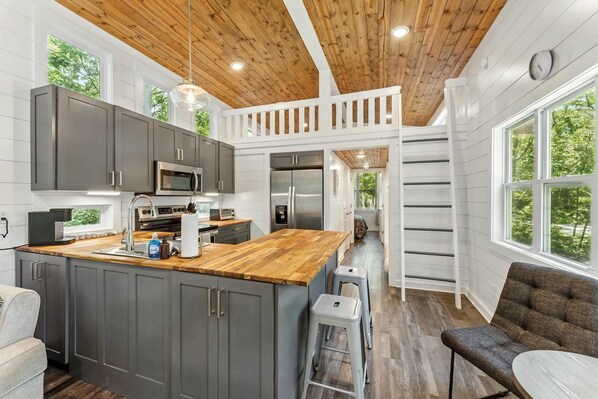 Una cocina moderna con armarios grises, una isla de madera y un comedor en un entrepiso.