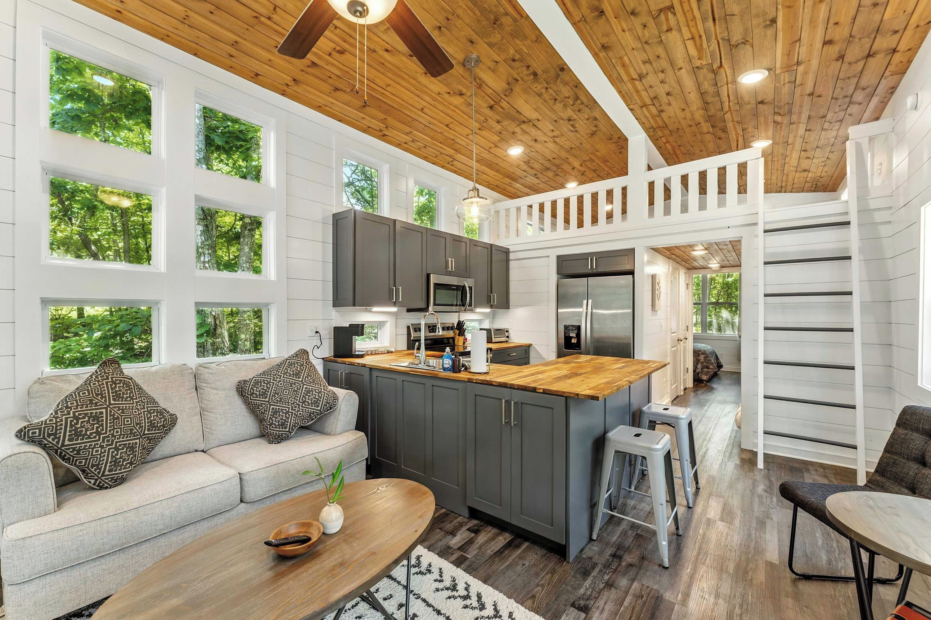 A modern kitchen with a central island, grey cabinets, and a wooden ceiling.