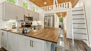 A modern kitchen with wooden ceiling, white cabinets, stainless steel appliances, and a wooden island.