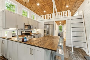 A modern kitchen with wooden ceiling, white cabinets, stainless steel appliances, and a wooden island. - Family getaway in Menlo, GA (Menlo)