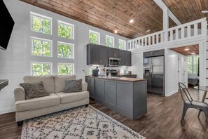 A modern kitchen with grey cabinets, a central island, and a dining area with a chair. - Family getaway in Menlo, GA (Menlo)