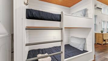 A bunk bed with a wooden ladder, a desk with a chair, and a window in a room with white walls and wooden flooring.