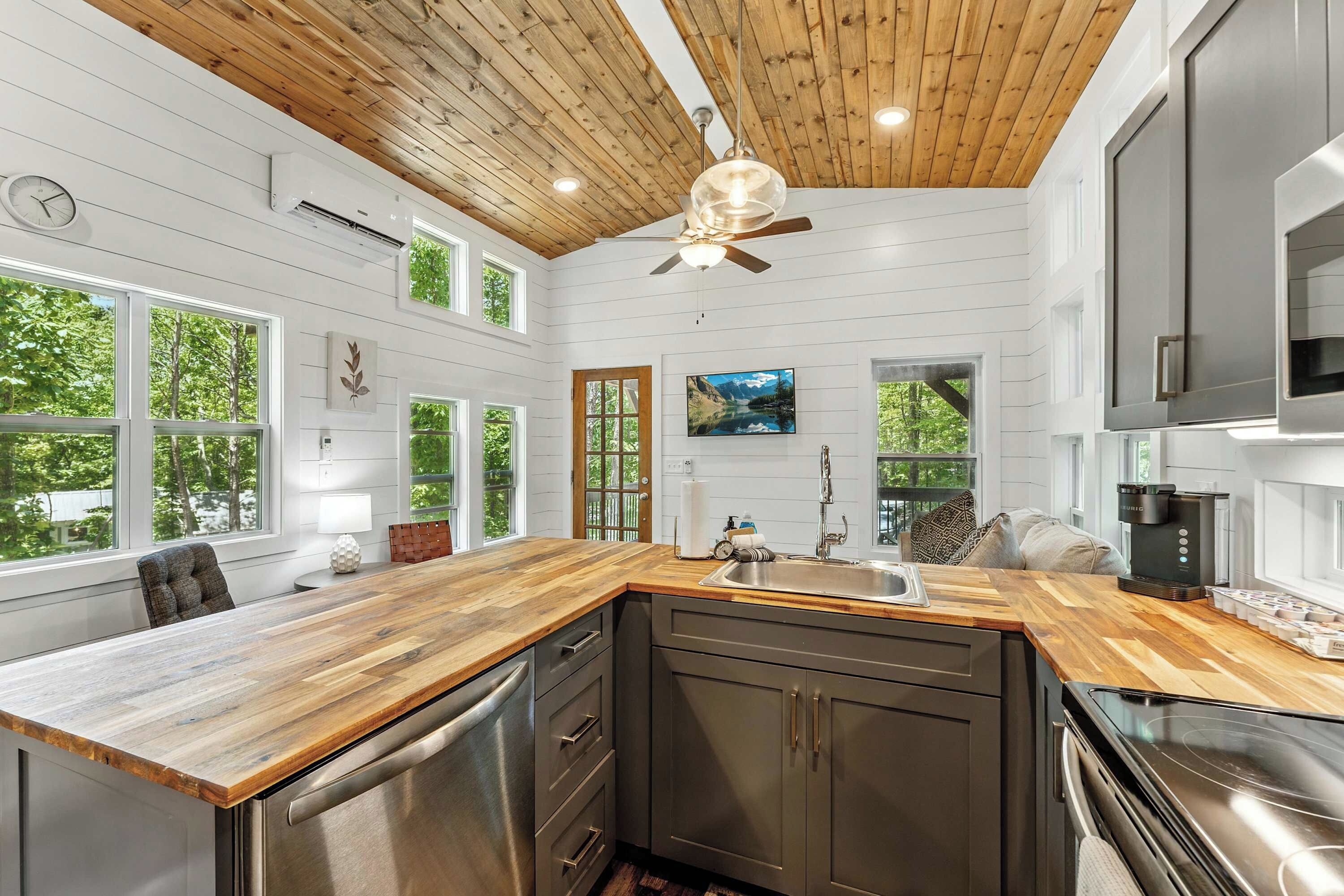 A modern kitchen with a wooden ceiling, large windows, and a built-in dishwasher.