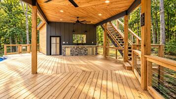 A spacious deck with a ceiling fan, a kitchen area with a refrigerator, and a staircase leading to an upper level.