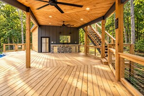 A spacious deck with a ceiling fan, a kitchen area with a refrigerator, and a staircase leading to an upper level. - Family getaway in Menlo, GA (Menlo)