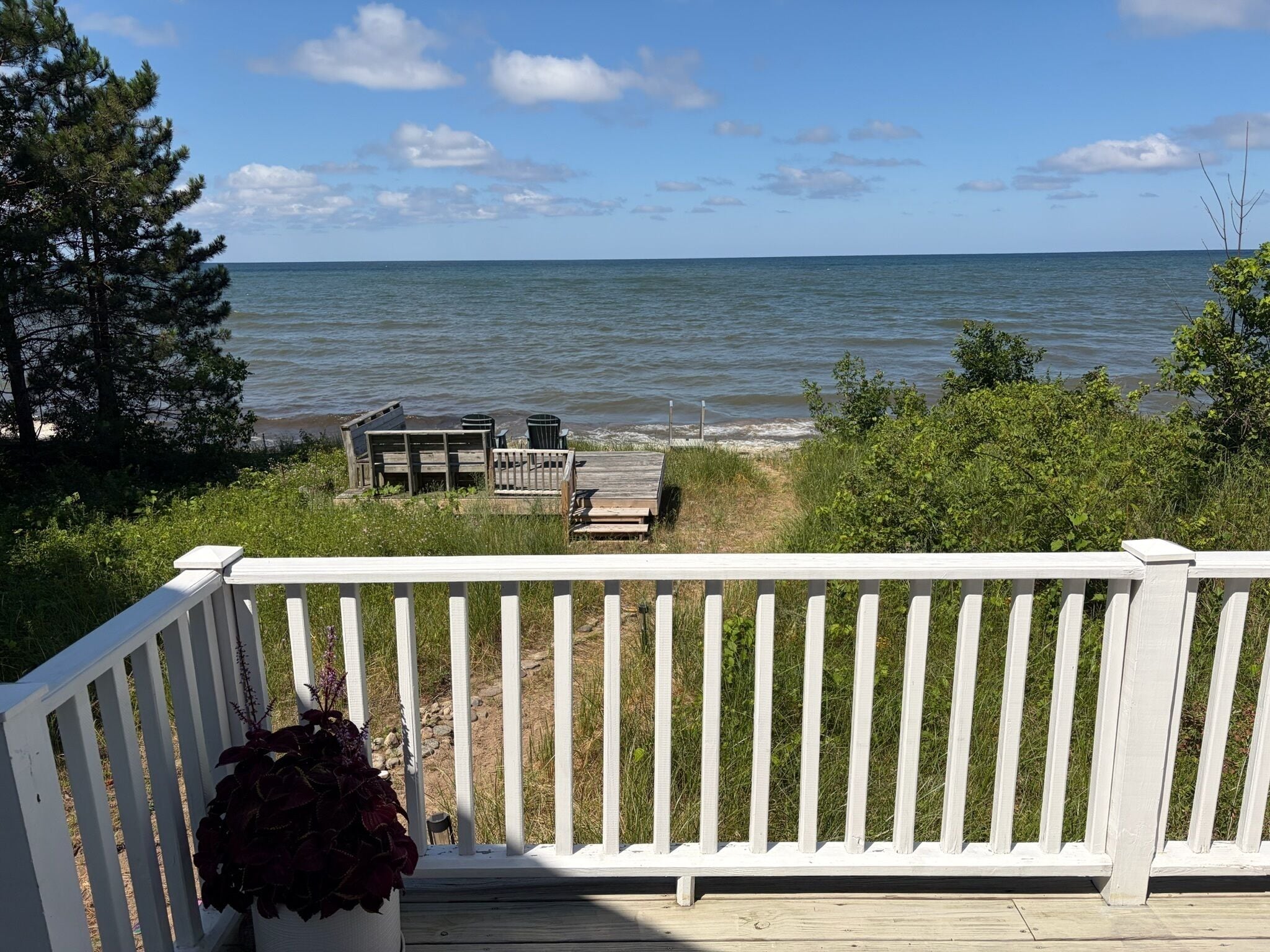A wooden deck with a white railing overlooking a body of water, a small dock, and a potted plant.