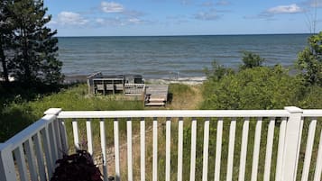 A wooden deck with a white railing overlooking a body of water, a small dock, and a potted plant.