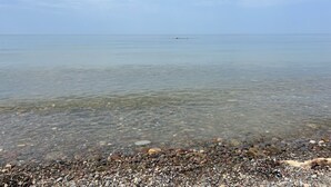 Ein kiesiger Strand mit klarem Wasser und einem entfernten Boot.