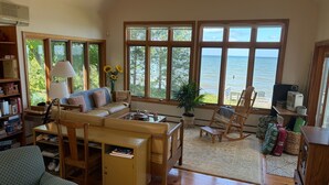 Ein geräumiges Wohnzimmer mit großem Fenster mit Meerblick, einer gemütlichen Sitzecke und einem Bücherregal voller Bücher.