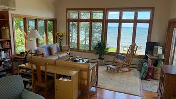 A spacious living room with a large window overlooking the sea, a cozy seating area, and a bookshelf filled with books.
