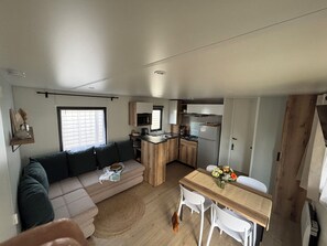 Ein kompakter Wohnbereich mit Sofa, Esstisch, Küchenzeile und Fenster.