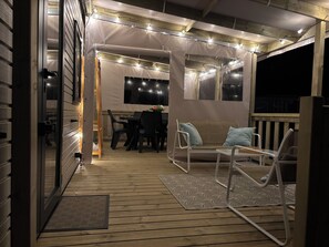 Ein Außenbereich mit einer Holzterrasse, einem Esstisch mit Stühlen, einer Sitzecke und Lichterketten.