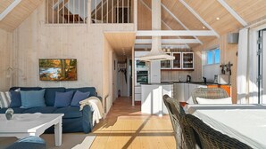 Ein geräumiger Loft-Raum mit hohen Decken, einer gemütlichen Sitzecke mit blauem Sofa und weißem Couchtisch, einem Essbereich und einer dahinterliegenden Küche, sowie einem großen Fenster, das für natürliches Licht sorgt.