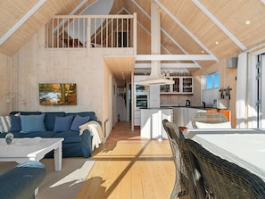 Un vaste espace de vie de style loft, doté d’un plafond haut, d’un coin salon confortable avec un canapé bleu et une table basse blanche, d’un coin repas avec une cuisine en arrière-plan et d’une grande fenêtre qui laisse entrer la lumière naturelle.