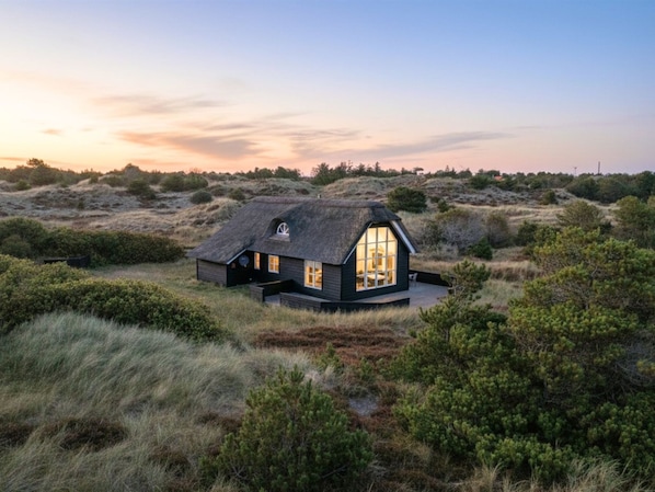 Une maison dotée d’une grande fenêtre, entourée d’un paysage naturel.