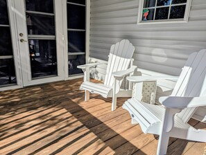 Eine überdachte Veranda mit Holzboden, weißen Adirondack-Stühlen und einem Fenster mit einem dekorativen Gegenstand.