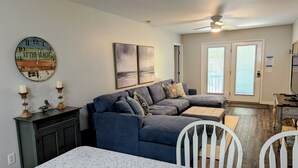 A living room with a sectional sofa, a dining table, and a kitchen area. - Turtleheart-Cozy 3BR 2BA in the heart of Oak Island, relax and enjoy island vibe (Oak Island)
