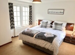 A neatly arranged bedroom with a bed, bedside tables, a lamp, and a window with curtains. - Sahara Park (No 11) | Elie (Elie)