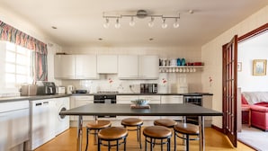 Una cocina moderna con una isla central, taburetes de bar, lavadora y un comedor con un sofá rojo.