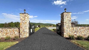 A paved pathway leading to a gated entrance with stone walls and lanterns on top. - Peaceful Lakefront 1BR 1 Full Bath w/ Private Island Access & Breakfast Included (Purcellville)