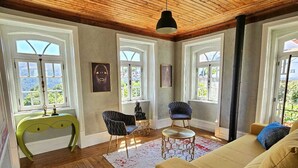 Ein geräumiges Wohnzimmer mit Holzböden, einer Couch, zwei Sesseln, einem Konsolentisch und einem Deckenventilator.
