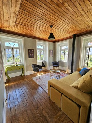 A spacious living room with wooden floors, a sofa, two armchairs, a console table, and a ceiling fan. - Casa da Júlia | Nature Refuge in Arganil (Folques)
