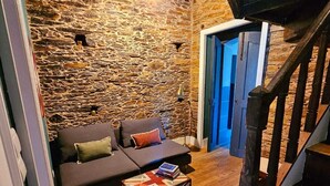 Ein gemütliches Wohnzimmer mit Steinwand, einer dunklen Couch, einem Holztisch und einer Treppe.