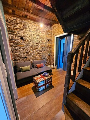A cozy living room with a stone wall, a dark sofa, a wooden coffee table, and a staircase. - Casa da Júlia | Nature Refuge in Arganil (Folques)