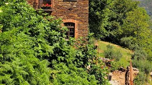 Ein Steinhaus mit Ziegeldach, zwei Fenstern und einem kleinen Balkon.