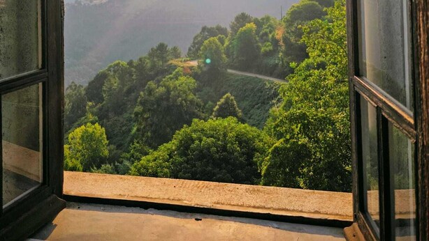 Ein offenes Fenster mit Blick auf eine gebirgige Landschaft und einen klaren Himmel.