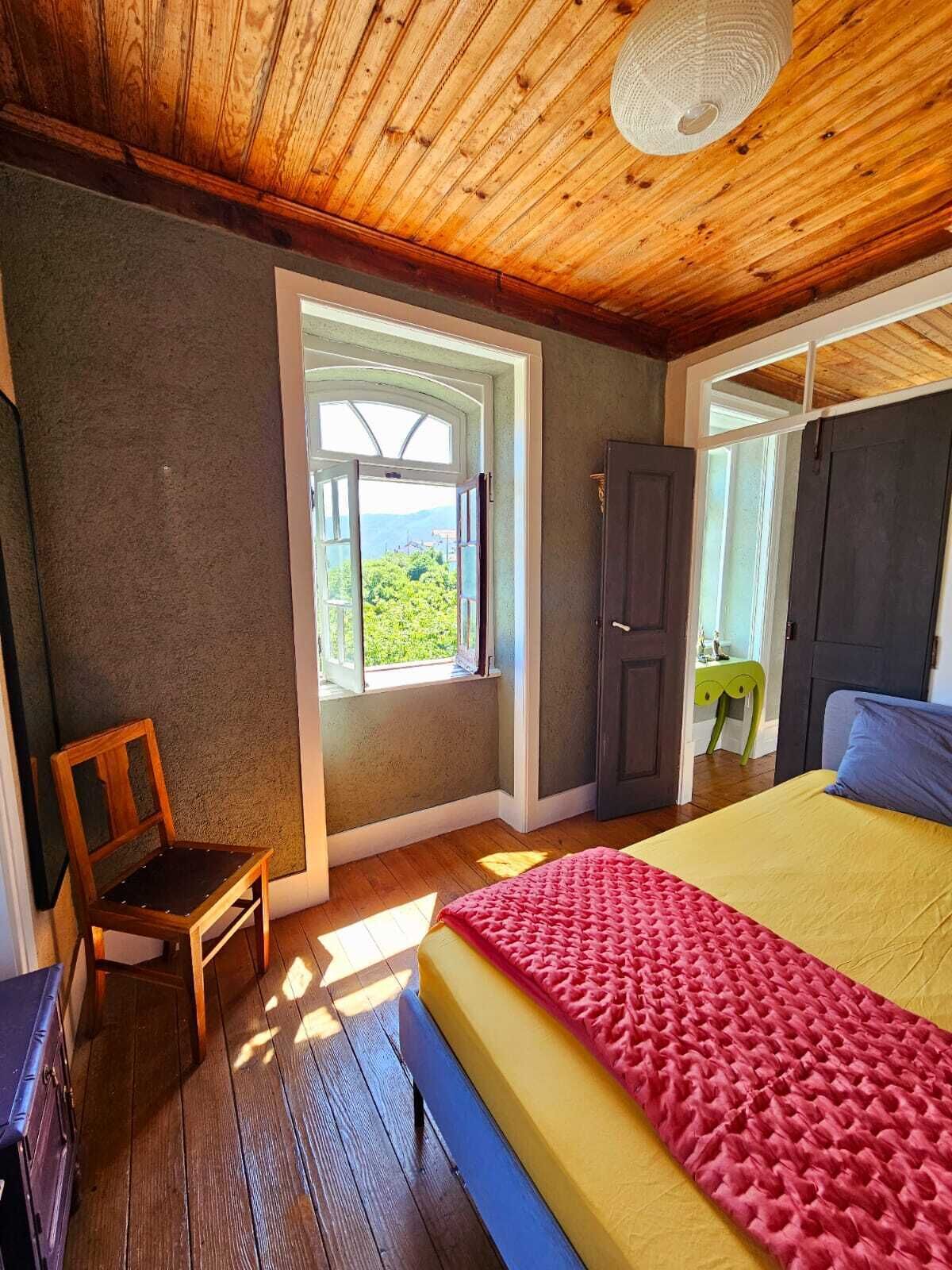 A bedroom with a bed, a chair, a wardrobe, and a window with a view.