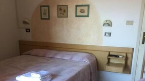A bedroom with a bed, a nightstand, a wall-mounted shelf, and a small table. - Hotel Maria Luisa (Rimini)
