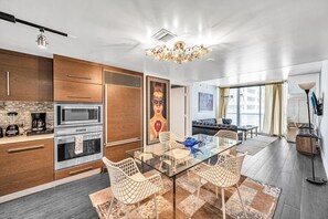 A modern kitchen with built-in appliances, a dining area with a glass table and wicker chairs, and a living room with a sofa and a large window. - Icon Brickell - 19th Fl - Oceanview - Spa Access (Miami)