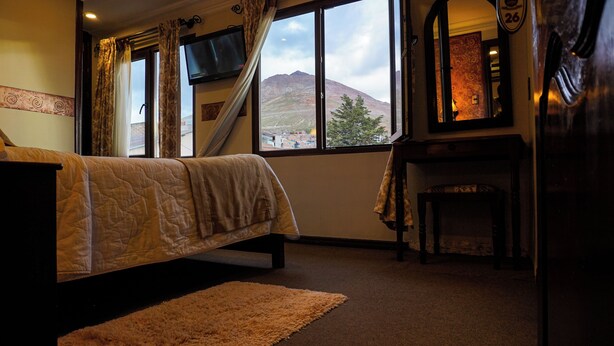 A bedroom with a bed, a TV, a desk, and a view of a mountain. - Cerro Rico Hotel with Garage - Breakfast Included (Villa Imperial de Potosí)