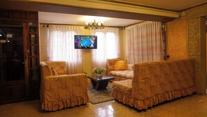 A living room with two armchairs, a sofa, a coffee table, and a TV on the wall. - Cerro Rico Hotel with Garage - Breakfast Included (Villa Imperial de Potosí)